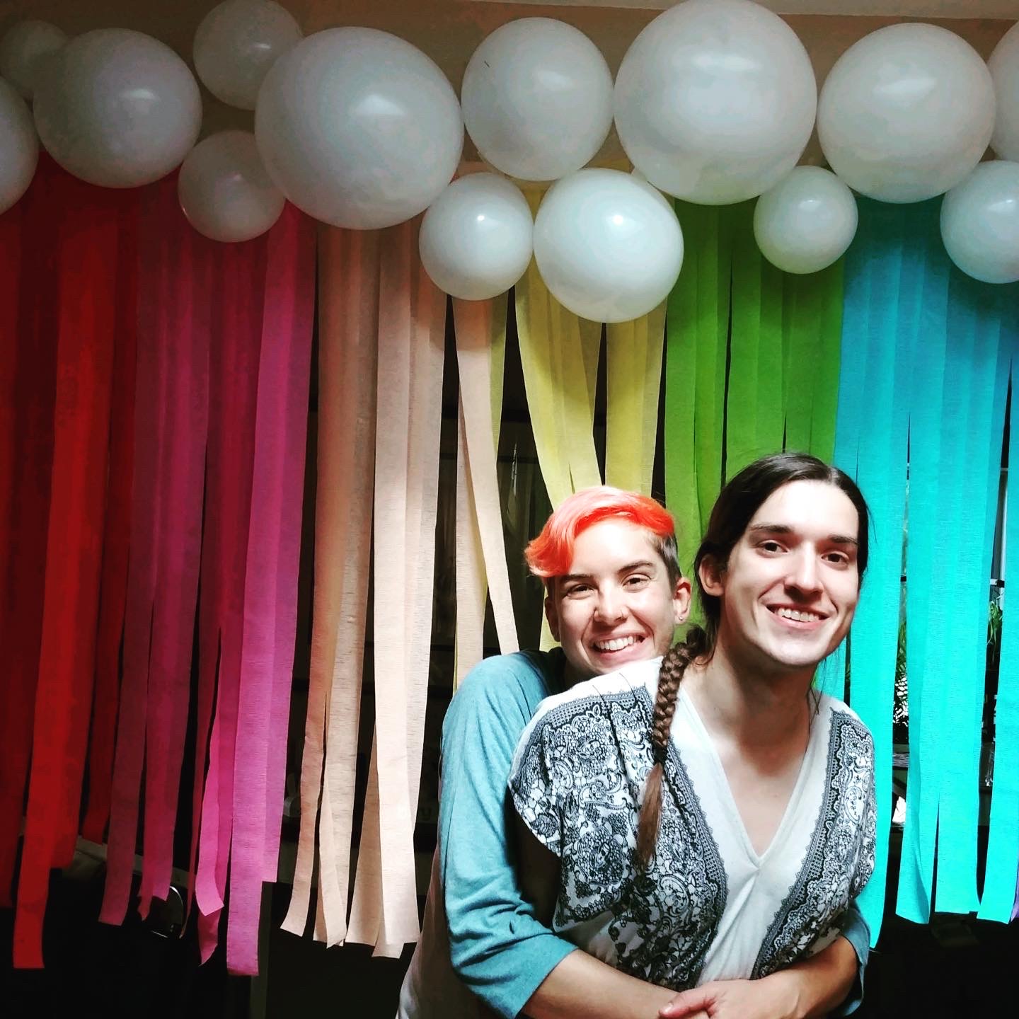 Mel and Teghan hugging in front of rainbow streamers